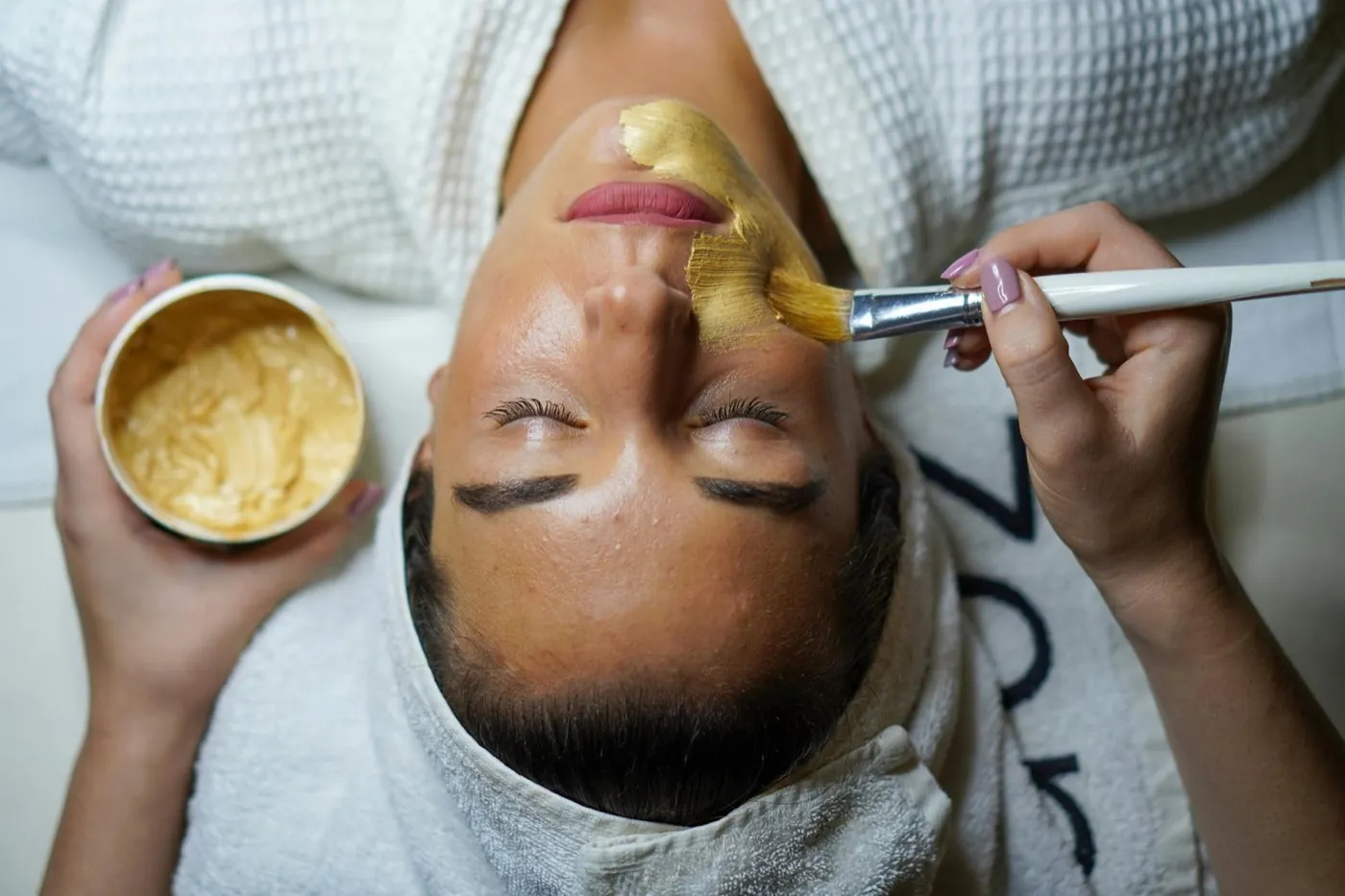 An aesthetician applying a gold mask during a facial